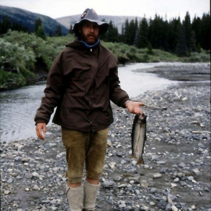 Mann mit Hut hält an einem Fluss einen gefangenen Fisch