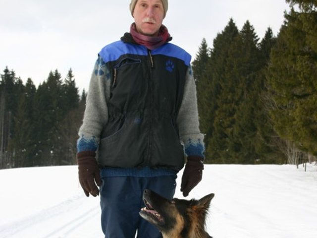 Mann steht im Schnee, ein Schäferhund sitzt vor ihm